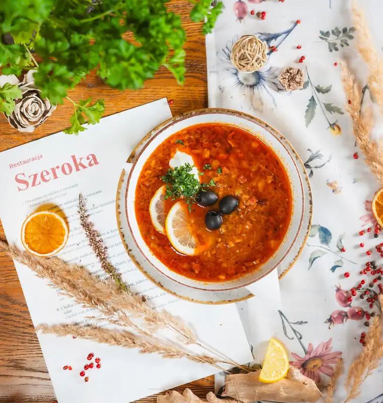 Solanka z cytryną i oliwkami na kwiecistym obrusie obok karty z napisem Szeroka